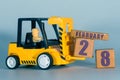 february 28th. Day 28 of month, Construction or warehouse calendar. Yellow toy forklift load wood cubes with date. Work planning