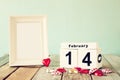 February 14th wooden vintage calendar with colorful heart shape chocolates next to blank vintage frame on wooden table