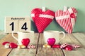 February 14th wooden vintage calendar with colorful heart shape chocolates next to couple cups on wooden table. selective focus Royalty Free Stock Photo