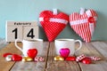 February 14th wooden vintage calendar with colorful heart shape chocolates next to couple cups on wooden table. selective focus Royalty Free Stock Photo