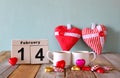 February 14th wooden vintage calendar with colorful heart shape chocolates next to couple cups on wooden table. selective focus Royalty Free Stock Photo