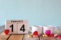 February 14th wooden vintage calendar with colorful heart shape chocolates next to couple cups on wooden table. selective focus Royalty Free Stock Photo