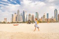 Cheerful woman in a sundress walks along the Persian Gulf coast with a backdrop of huge skyscrapers