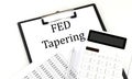 FED TAPERING text on folder with chart and calculator on white background