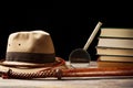 Fedora hat with bullwhip near magnifying glass and old books on black background. Adventure concept Royalty Free Stock Photo