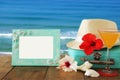 Fedora hat, tropical hibiscus flower next to blank frame over wooden table and beach landscape background Royalty Free Stock Photo