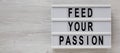 `Feed your passion` words on a lightbox on a white wooden background, top view. Overhead, from above, flat lay. Copy space