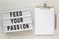 `Feed your passion` words on a modern board, clipboard with blank sheet of paper on a white wooden background, top view. Overhea