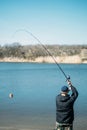 Feeder fishing. Male fisherman fishing at sun day on the lake. Man in jacket catches bream fish in early spring. Fishing hobby