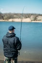 Feeder fishing. Male fisherman fishing at sun day on the lake. Man in jacket catches bream fish in early spring. Fishing hobby