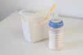 A feeding bottle with baby formula milk on white table, dry powder milk in a can in background Royalty Free Stock Photo