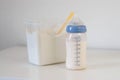 A feeding bottle with baby formula milk on white table, dry powder milk in a can in background Royalty Free Stock Photo