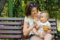 Feeding kid outdoor: infant baby sitting on knees of his mother in summer park and eating vegetable puree from a spoon Royalty Free Stock Photo