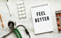 FEEL BETTER is written in a notebook on a white table next to pills and a stethoscope Royalty Free Stock Photo