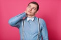 Portrait of attractive young man in blue shirt, suspenders and white bow tie touching his neck and looks pensive while standing Royalty Free Stock Photo