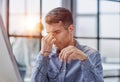 Frustrated young man massaging his nose and keeping eyes closed while sitting at his working place in office Royalty Free Stock Photo