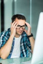 Feeling sick and tired. Frustrated young man massaging his nose and keeping eyes closed while sitting at his working place in Royalty Free Stock Photo