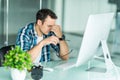 Feeling sick and tired. Frustrated young man massaging his nose and keeping eyes closed while sitting at his working place in Royalty Free Stock Photo