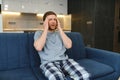 Feeling stressed. Frustrated handsome young man touching his head and keeping eyes closed while sitting on the couch at Royalty Free Stock Photo