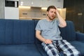 Feeling stressed. Frustrated handsome young man touching his head and keeping eyes closed while sitting on the couch at Royalty Free Stock Photo