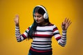 Emotional young cute girl, student in warm clothes listening to music in headphones isolated on yellow color studio