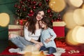 They feels the satisfaction being together these holidays. Cheerful mother and daughter sitting near the Christmas tree that