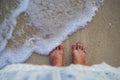 Feet on beach background. Top view on naked feet and legs in sand with wave motion coming to the foot - foaming sea texture. Royalty Free Stock Photo