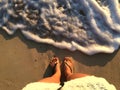 Feet on beach background. Top view on naked feet and legs in sand with wave motion coming to the foot - foaming sea texture. Royalty Free Stock Photo