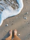 Feet on beach background. Top view on naked feet and legs in sand with wave motion coming to the foot - foaming sea texture.