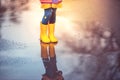 Feet of child in colorful rubber boots jumping over puddle in rain. Autumn park