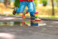 Feet of child in colorful rubber rain boots jumping over rainy puddle in a park Royalty Free Stock Photo