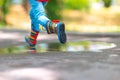 Feet of child in colorful rubber rain boots jumping over rainy puddle in a park Royalty Free Stock Photo