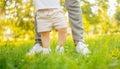 Feet of child in white shoes take first step, mother of parent hedges and helps. Sunlight summer concept