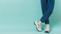 Feet of a child in white sneakers with laces and wide jeans on a blue background. Place for text. Royalty Free Stock Photo