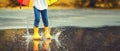 Feet of child in yellow rubber boots jumping over puddle in ra