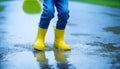 Feet of child in yellow rubber boots jumping over puddle in rain Royalty Free Stock Photo