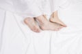 Feet of couple sleeping side by side in comfortable bed. Close up of feet in a bed under white blanket. Bare feet of a Royalty Free Stock Photo