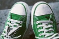 Feet in dirty green sneakers and jeans outdoors.