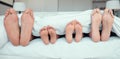 Feet of family lying in bed. Close up of feet of parents and two children in bed. Family relaxing in bed together. Below Royalty Free Stock Photo