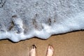 Feet on a fine sandy beach with beautiful waves.