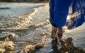 Feet of a girl in a skirt goes along the waves, glare of the sun on the water during sunset Royalty Free Stock Photo