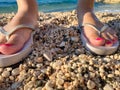 Feet Girl with a neat pedicure in women`s stylish beach flip-flops aqua on the beach background. Two sandals on the sand near the Royalty Free Stock Photo