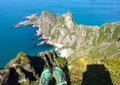 Feet in green sports shoes over the abyss, above the green rocky peninsula jutting out into the blue sea. Top view. Royalty Free Stock Photo