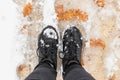 Feet of a human in sneakers walking on an snowy sidewalk in melty snow