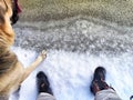 Feet of Hunter or fisherman in big warm boots And paws of dog on snow. Top view. Fisherman on ice of river, lake