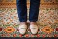 feet in leather slippers standing on an embroidered mat