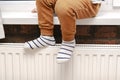 Feet legs of little boy kid in warm socks.Child sitting by window and warming up from heat radiator.Centralized heating