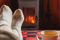 Feet legs in winter clothes wool socks and cup tea at fireplace at home on winter or autumn evening relaxing and warming up Royalty Free Stock Photo