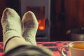 Feet legs in winter clothes wool socks and cup tea at fireplace at home on winter or autumn evening relaxing and warming up Royalty Free Stock Photo