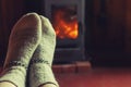 Feet legs in winter clothes wool socks at fireplace background. Woman sitting at home on winter or autumn evening relaxing and